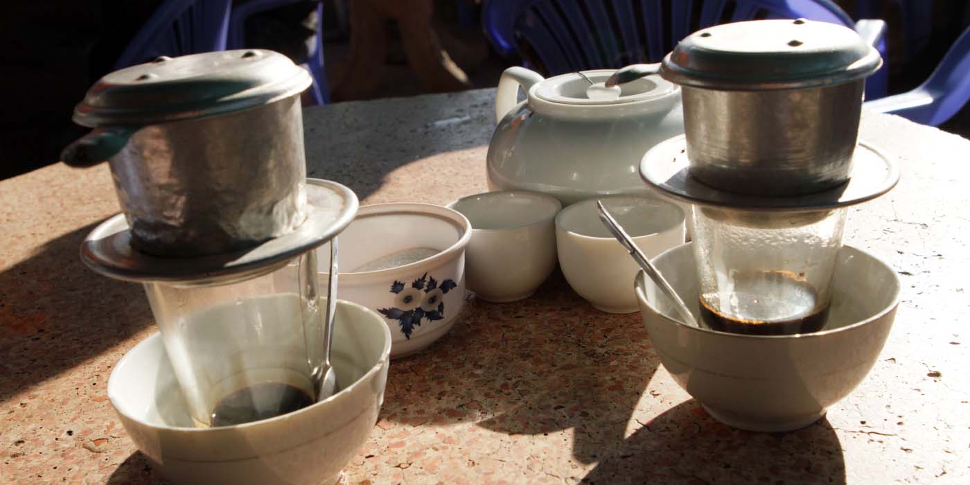 Two Vietnamese coffees being prepared with a phin filter into glass cups.
